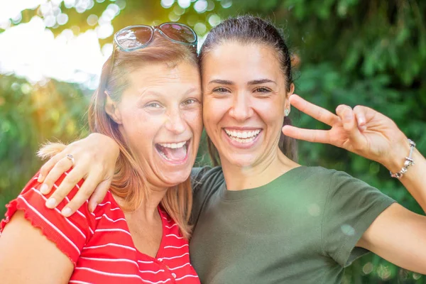 Dos amigas felices riendo juntas en un parque con un verde — Foto de Stock