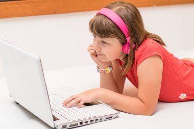 Güzel bir öğrencinin portresi, internetteki video dersleri, kulaklıklar ve evdeki kanepede uzanan bir bilgisayar.
