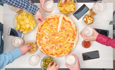 Bir grup arkadaş evde dinlenirken bira içiyor, pizza yiyor, konuşuyor ve gülümsüyor.