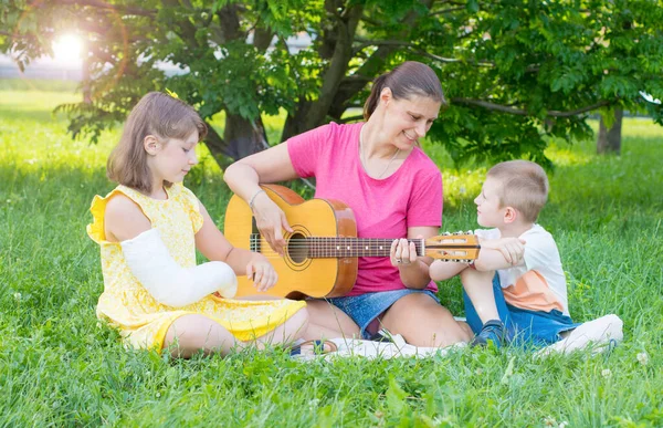 妈妈和她的两个孩子在公园里弹奏吉他 放松和户外生活的概念 — 图库照片