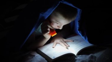 Küçük çocuklar yatak örtüsünün altında kitap okuyorlar.