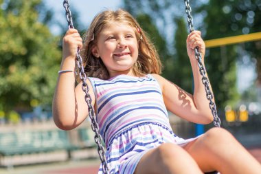 Gülümseyen kız parkta salıncakta sallanıyor.