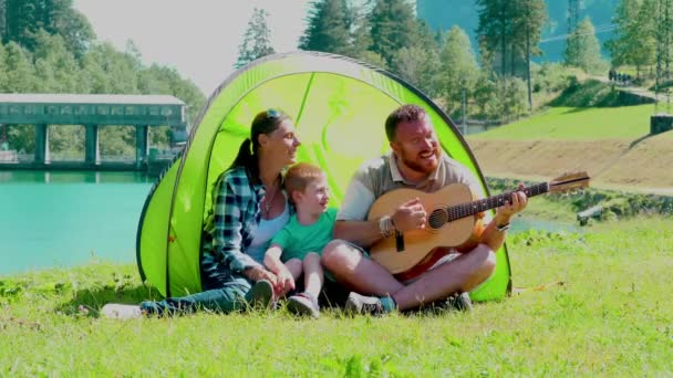 Szczęśliwa Rodzina Namiotem Gra Gitarze Śpiewa Razem Przed Górskim Jeziorem — Wideo stockowe