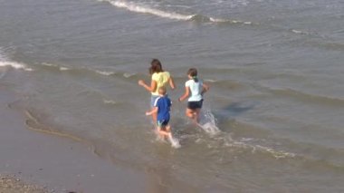 Anne ve çocuklar plajda birlikte koşuyorlar.