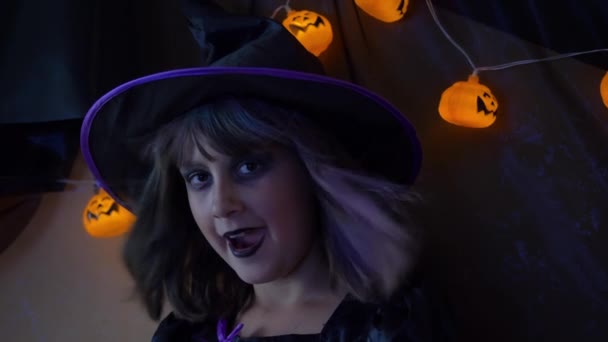 明るいカボチャに囲まれた魔女の格好をした若い女の子はハロウィンを祝う — ストック動画