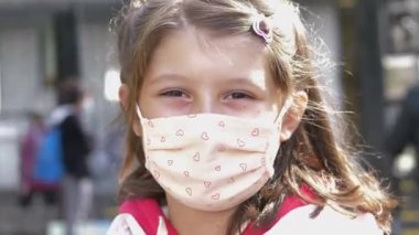 Okulun önündeki genç öğrenci kameraya bakar. Koronavirüsü önlemek için maske takar.