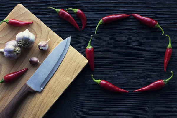 Nóż czosnek drewniany deska chili na ciemnym tle — Zdjęcie stockowe
