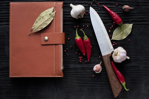 Cuchillo de chef ajo chile y bloc de notas en un fondo oscuro de madera — Foto de Stock