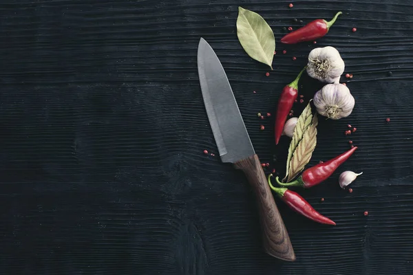 Szef kuchni nóż czosnek czerwona papryka chili na czarnym drewnianym tle — Zdjęcie stockowe