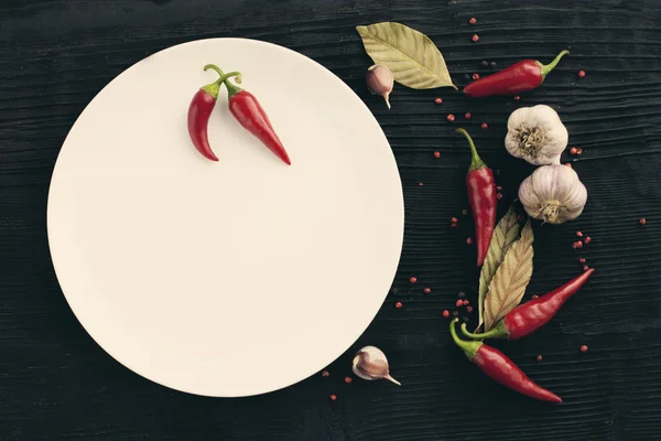 Biała płyta czosnek czerwona papryka chili na czarnym drewnianym tle — Zdjęcie stockowe