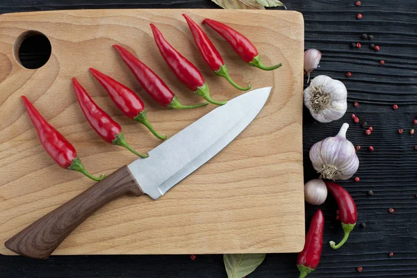 Grande chef coltello aglio bordo di legno chili su uno sfondo scuro — Foto Stock