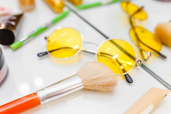 Accessories for the stylist such as yellow fashion glasses, makeup brushes