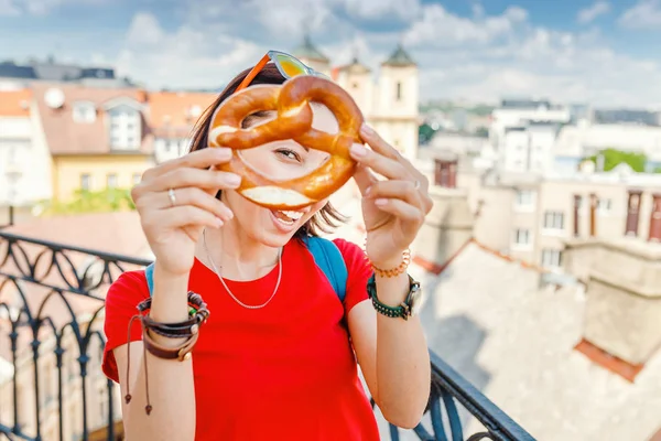 A female hand holds a traditional bakery and a pretzel delicacy against the background of the historic center of the European city