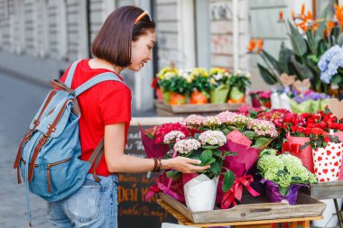 Bir kadın alıcı seçer ve sokakta bir çiçek dükkanında satın almadan önce buketleri kokuyor