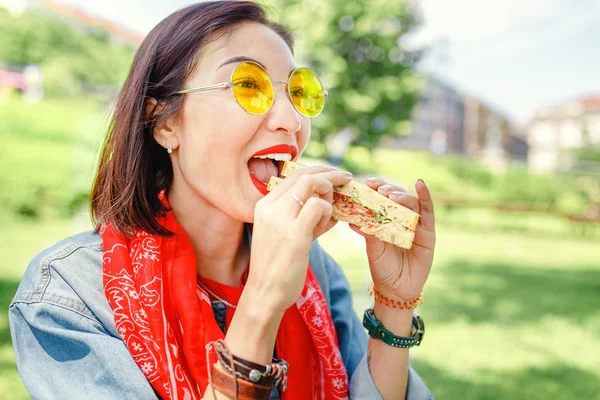 Genç kadın yeme sandviç ve öğle yemeği Park'ta açık havada kırmak