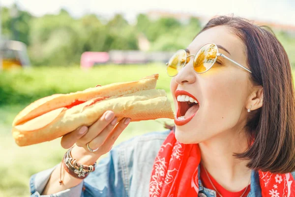 Young woman eating sandwich and having lunch break outdoors in park