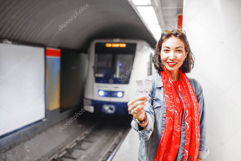 The woman shows two tickets at the background of the approaching train in the subway. Concept of urban public underground transport