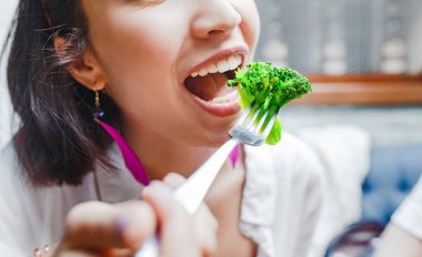 Portrait of happy smiling young casual woman eating broccoli in restaurant clipart