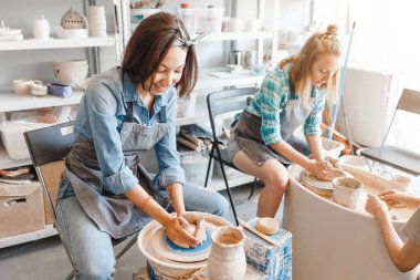 Gülümseyen ve clay craft el yapımı çanak çömlek atölyesi, dostluk ve rehberlik kavram yapma potters tekerlek üzerinde çalışırken konuşmak iki kız arkadaş