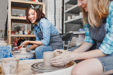 Gülümseyen ve clay craft el yapımı çanak çömlek atölyesi, dostluk ve rehberlik kavram yapma potters tekerlek üzerinde çalışırken konuşmak iki kız arkadaş