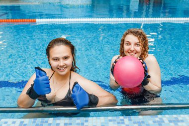 İki mutlu kız havuzda spor ve fitness aqua aerobik topu ve eldiven kullanarak nişanlandık