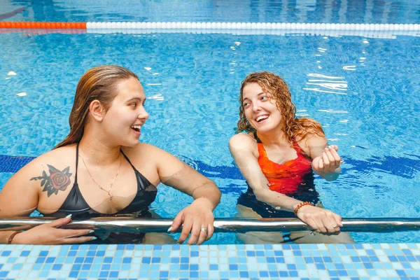 Two fit sporty women talking at the border of swimming pool