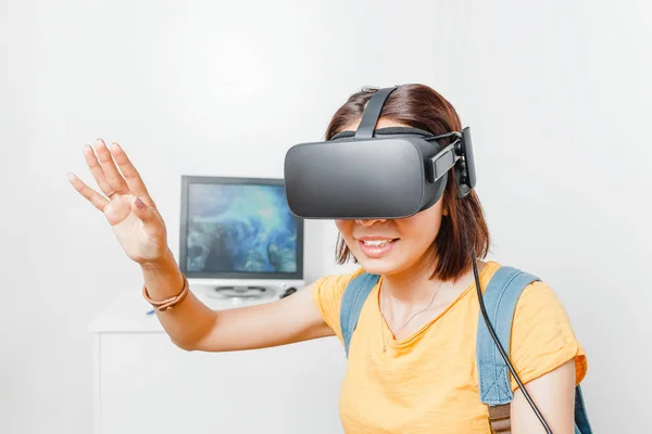 Woman playing video game with virtual reality VR headset against computer monitor