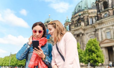 İki kız arkadaş gezgin Berlin şehri yürürken cep telefonu app kullanarak. Wi-fi internet bağlantısı Europe kavram