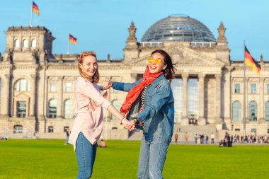 İki genç öğrenci kızlar eğleniyor ve dans ve Berlin - Bundestag ünlü dönüm noktası yakınındaki çimenlerin üzerinde piggybacking bina. Seyahat kavramı