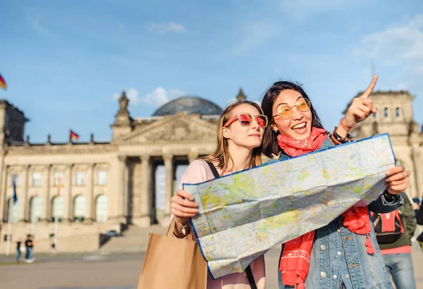 Multiracial group of friends visiting the city of Berlin. Two women reading map with Reichstag building on the background. Friendship and travel concept with real candid emotions