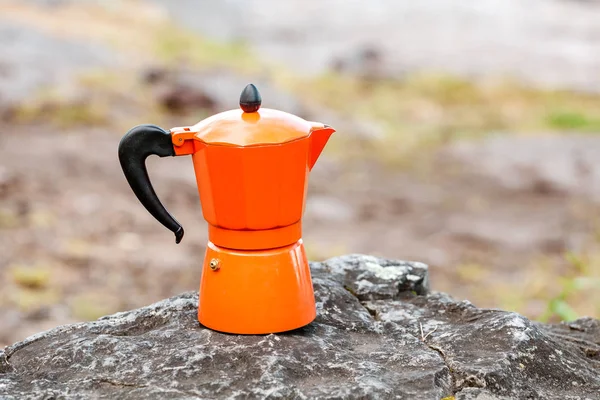 Coffeepot with hot coffee standing on a rocky cliff outdoors. Hiking and camping kitchen utensils and gear concept