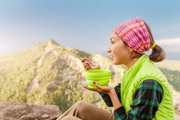 Woman hiker eating meal from plate while camping in mountains