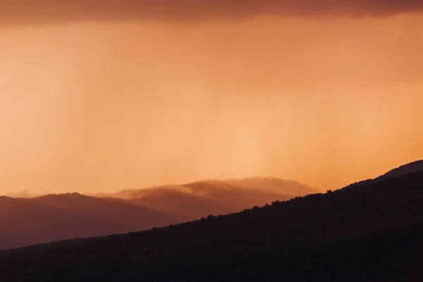 Rain in mountain landscape with clouds at sunset