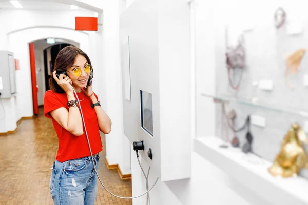 Asian Woman looking at museum exhibition, and listening audio guide using headphones in modern gallery. Education and leisure concept