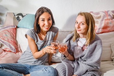 Neşeli genç kız kanepe kendi evinde şarap bardakları toasting arkadaşlar