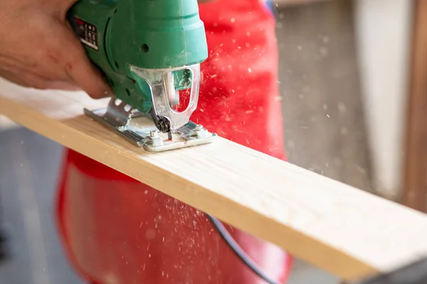 Close-up on worker cutting out a patterned contour on a wooden board using an electric jigsaw with a laser guide