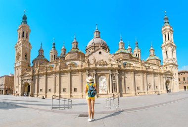Young happy woman tourist walking near the famous cathedral Del Pilar on the central square during summer vacation in Zaragoza city, Aragon, Spain clipart