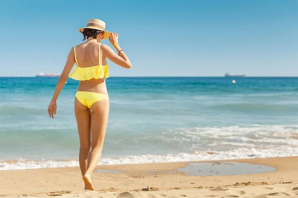 Happy smiling young woman in sun hat walking on beach along seaside, summer sea vacation and travel concept