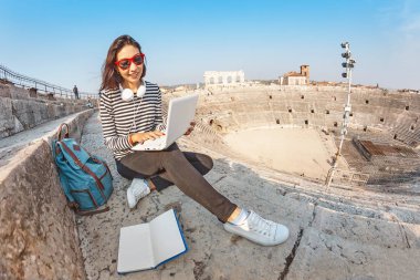 Mutlu Asyalı kız öğrenci dizüstü pc veya serbest çalışma Avrupa Simgesel Yapı amfitiyatro otururken, ödevlerini yapıyor. Tatil ve eğitim kavramı