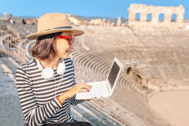 Mutlu Asyalı kız öğrenci dizüstü pc veya serbest çalışma Avrupa Simgesel Yapı amfitiyatro otururken, ödevlerini yapıyor. Tatil ve eğitim kavramı