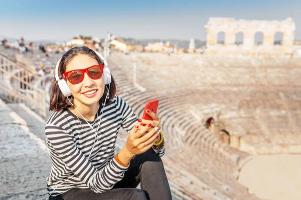 Щаслива Азіатська Жінка Сидить Всередині Стародавнього Амфітра Смартфоном Слухаючи Музику — стокове фото