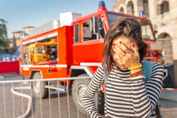 A woman in stress covers her face with her hands on the background of a fire fighting truck. Accident and insurance concept