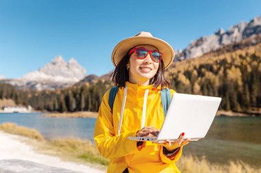 Sonbaharda laptop dağ gölü arka plan üzerinde çalışan mutlu Asyalı kadın. Uzaktan çalışma ve freelancer kavramı
