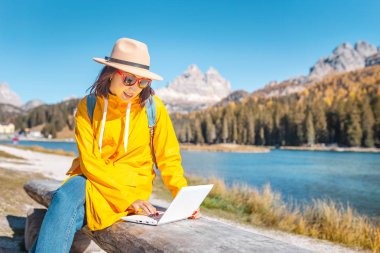 Sonbaharda laptop dağ gölü arka plan üzerinde çalışan mutlu Asyalı kadın. Uzaktan çalışma ve freelancer kavramı