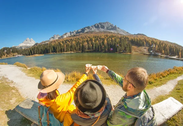 Happy three friends travel in Italian Dolomites mountains drinking tea on the coast of a Misurina Lake