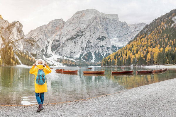 Asian woman traveler on the shore of the famous tourist lake Braies in the Dolomites Alps, Italy. The concept of travel and adventure in the mountains at autumn season