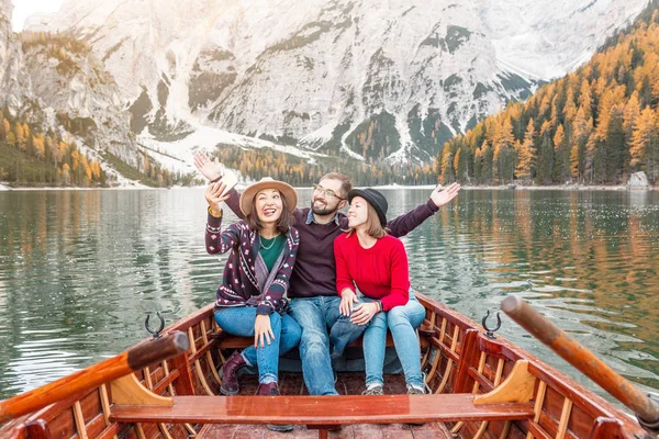 Group of three happy travelers on a wooden Boat on a lake in the mountains. Vacation and tourism in Italian Dolomites concept