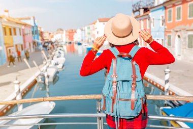 Venedik, Burano adasındaki renkli evlerin arasında poz veren genç mutlu gezgin kadın. İtalya 'da turizm kavramı