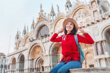Genç Asyalı kız mutlu traveler şapka ve Venedik'te San Marco meydanında parapetin üzerinde oturan sırt çantası. Tatil ve tatil İtalya ve Avrupa kavramı