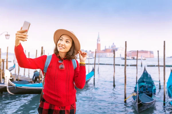 Young female traveler girl making selfie photo at the San Marco square with gondolas on the background. Travel in Venice concept